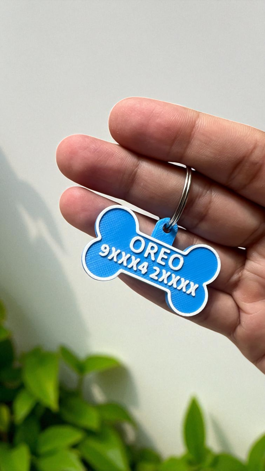 Hand holding a blue pet tag with custom text and numbers on a white background