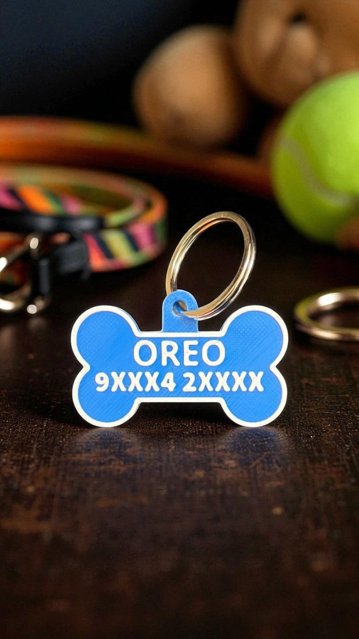 Blue bone-shaped pet tag with 'OREO' and identification numbers on a wooden surface with pet accessories.